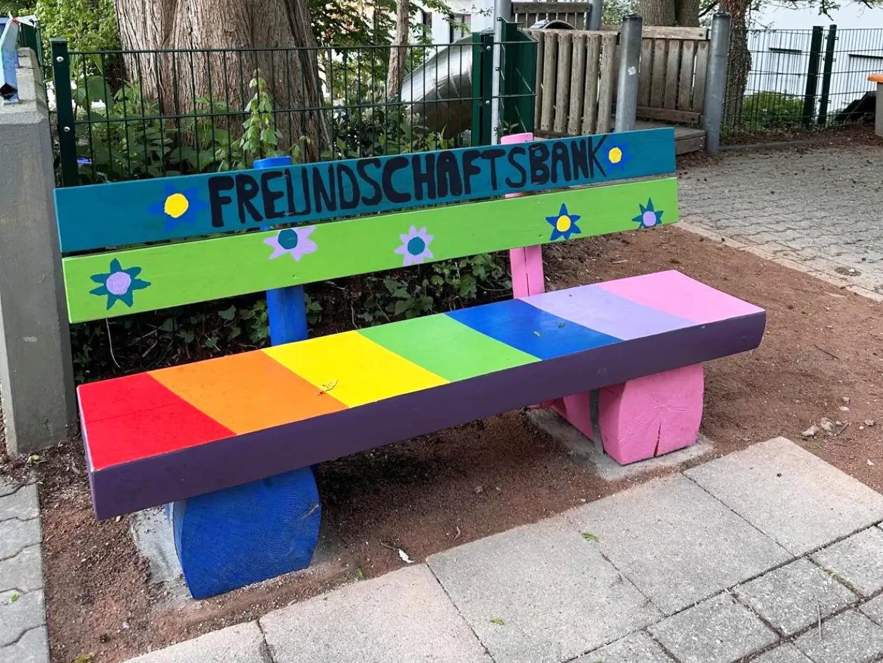 Das Bild zeigt eine bunte Bank auf einem Schulhof